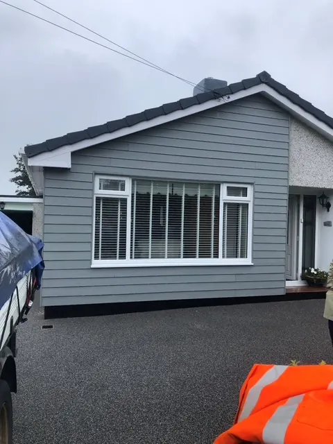 Bungalow clad in grey boards, with white render on the side wall and a dark driveway. One of our jobs.