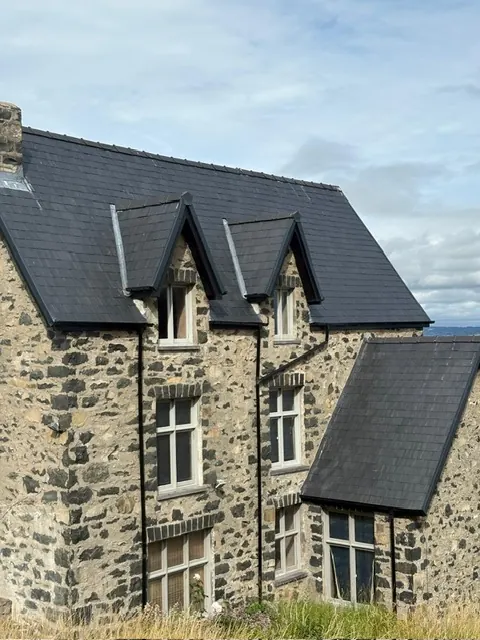 Stone house with a new dark slate roof and three slate-hung dormer windows. One of our jobs.